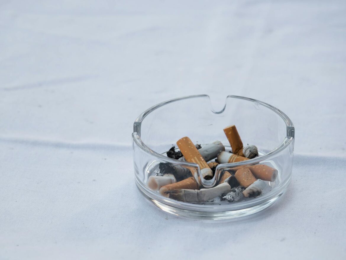 A clear glass ashtray filled with cigarette butts and ash placed on a white surface.